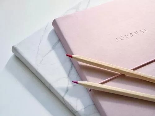 a pink and a white journal with pencils to craft a morning meditation routine