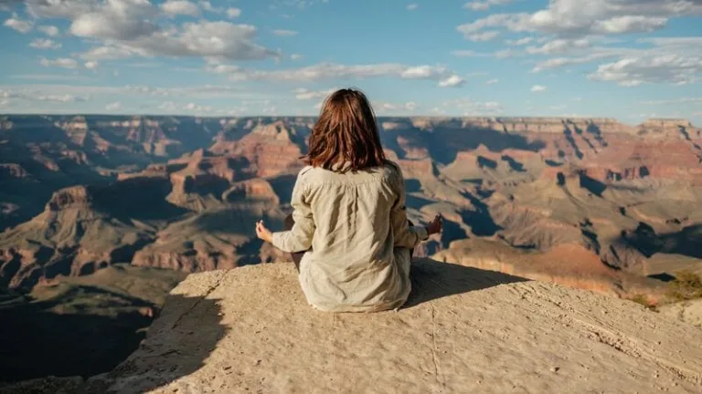 A woman practicing mindfulness meditation for overcoming the fear of change on top of a mountain.